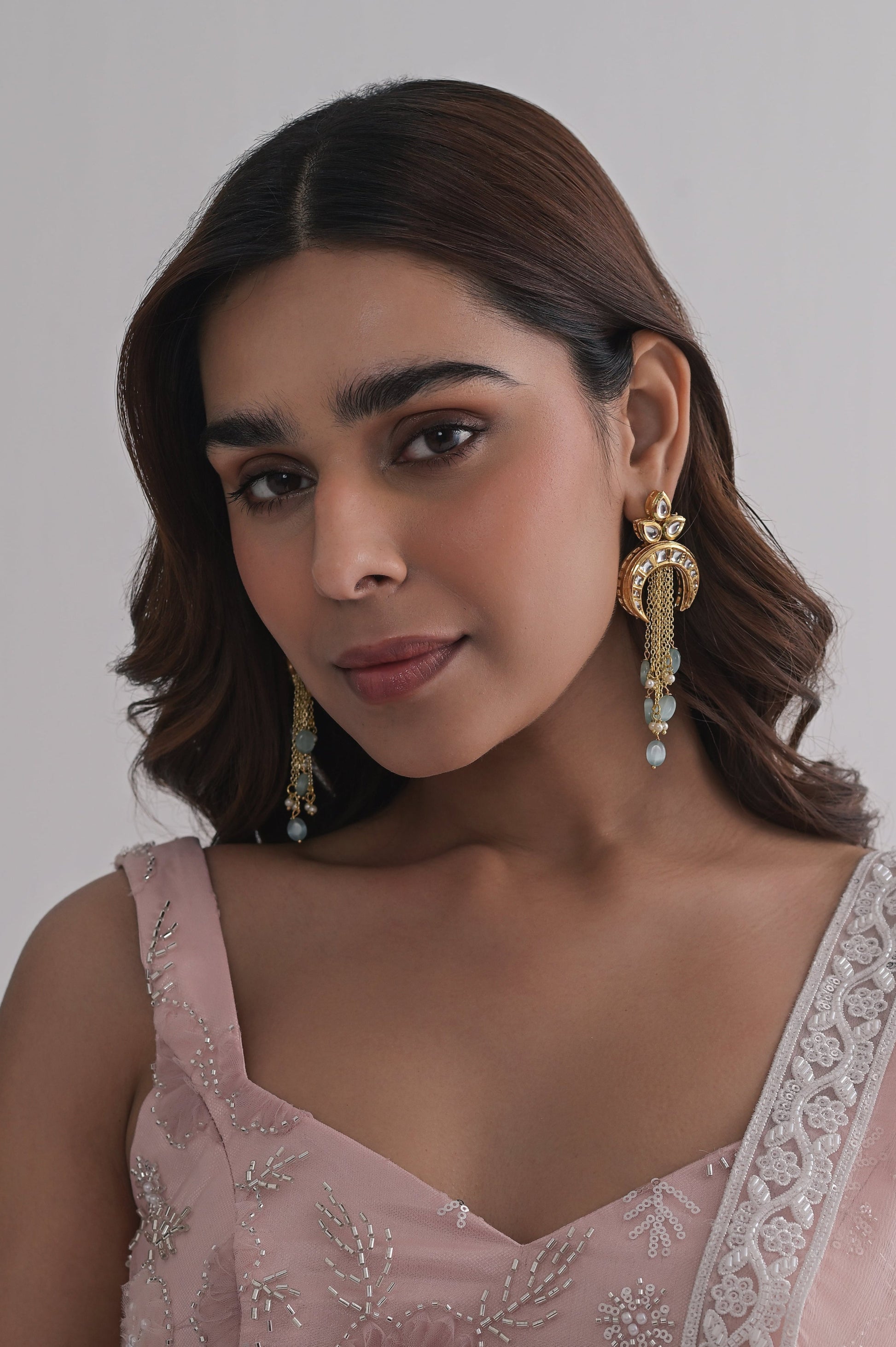 Statement crescent earrings in gold with kundan embellishments, floral top, and layered aqua bead tassels.