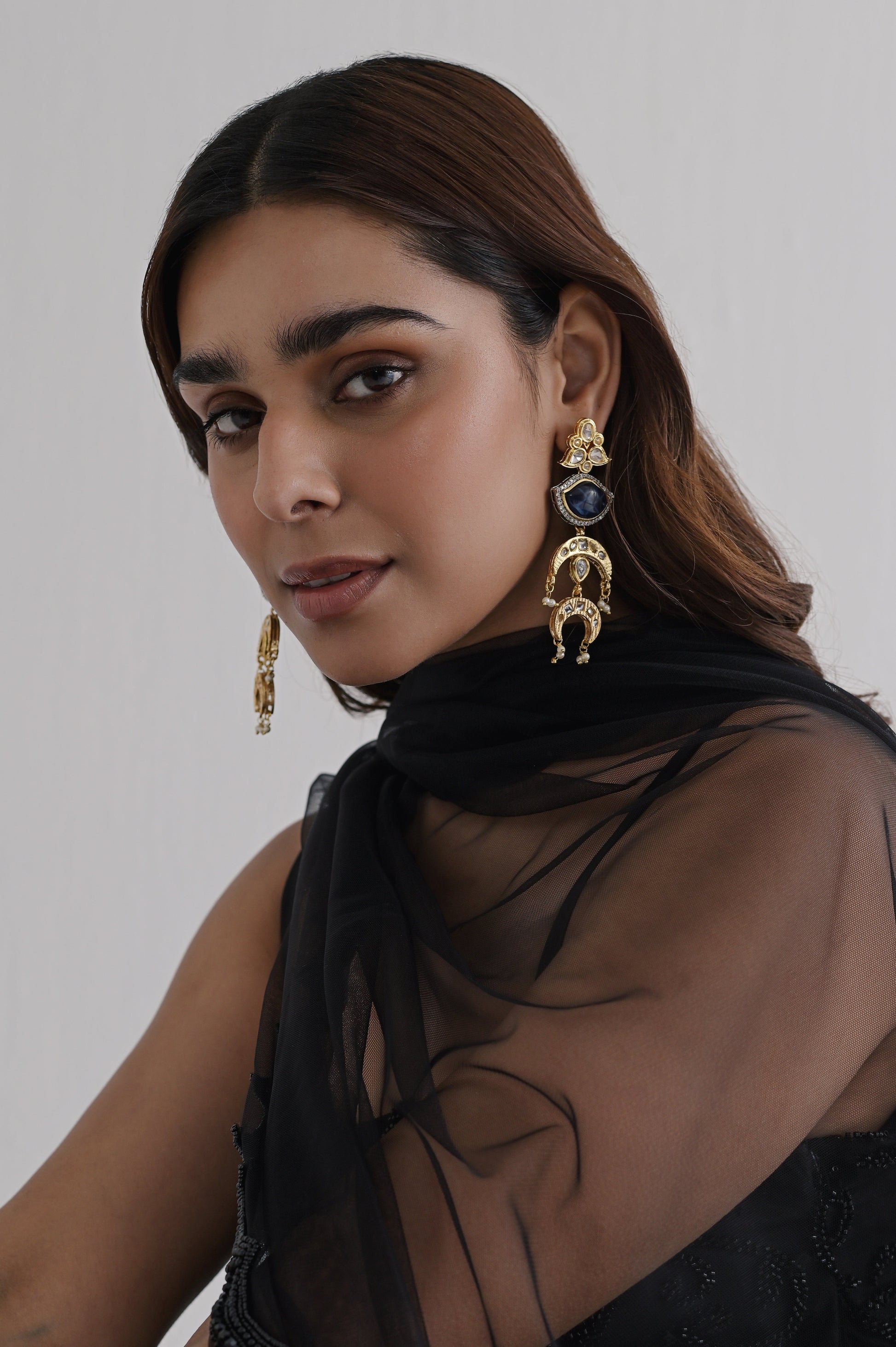 Gold-finished layered earrings featuring kundan work, delicate white stones, and a deep-hued teardrop accent stone surrounded by mini diamonds.